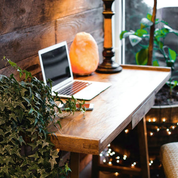 Wooden desk with laptop, salt lamp, and plants in a cozy room.
